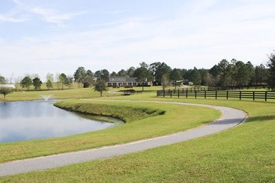 Green acreage with fenced pasture, a pond, and a home in the distance