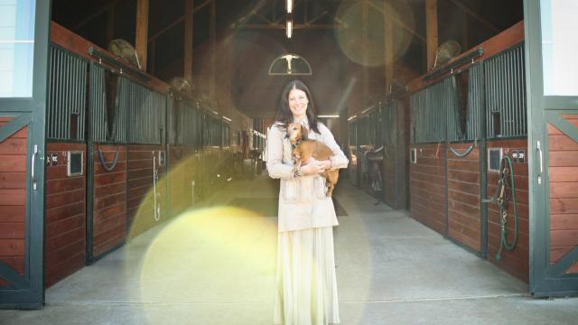 Mary Guynn holds her dog in the entrance to a horse barn